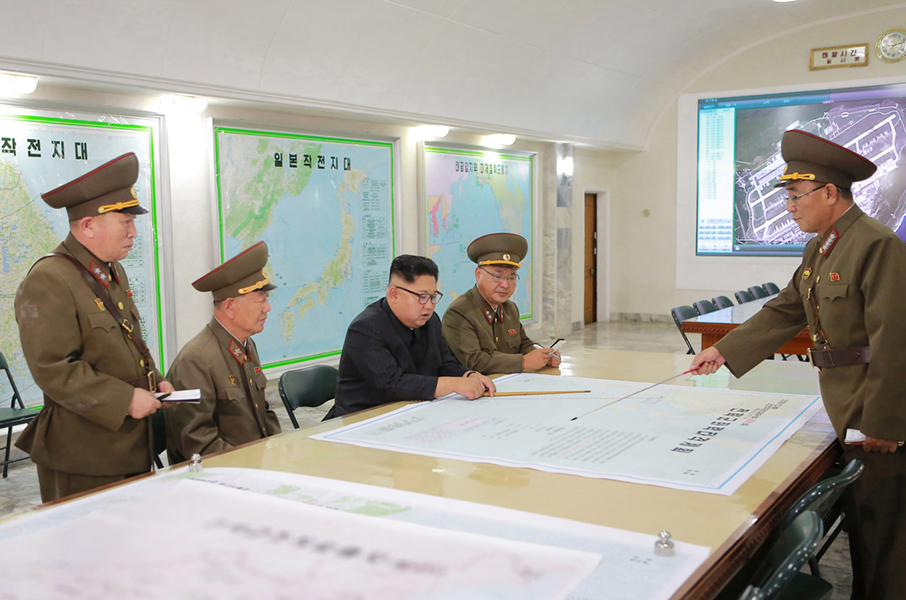 North Korean leader Kim Jong Un is shown reviewing plans for a missile strike near the U.S. territory of Guam in photo from the official Korean Central News Agency released August 15. The video monitor appears to show a satellite image of Andersen Air Force Base on Guam. (Photo credit: STR/AFP/Getty Images)