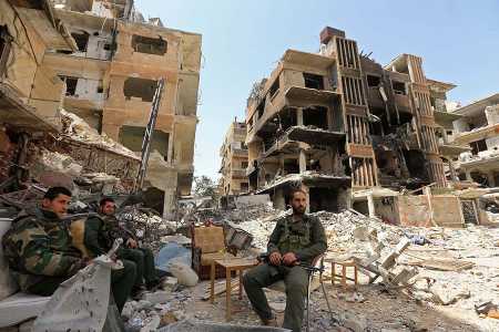 Syrian pro-government forces sit amid destroyed buildings in Douma on the outskirts of the Damascus on April 20, during an army-organized media tour. (Photo: LOUAI BESHARA/AFP/Getty Images)