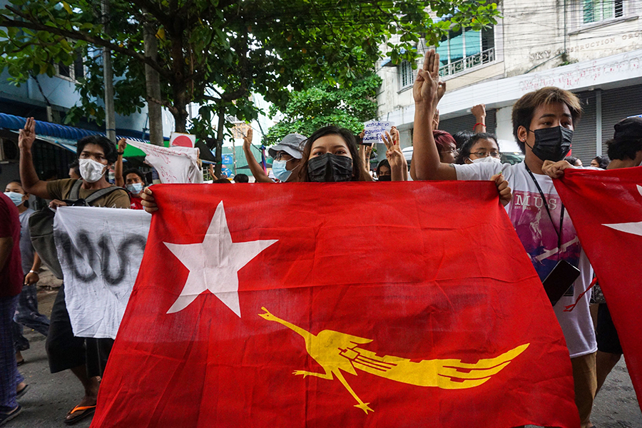 A protester holds the flag of the National League for Democracy, the party of jailed leader Aung San Suu Kyi, while making the three-finger salute during a flash mob demonstration against the military coup in Yangon on June 25. (Photo by STR/AFP via Getty Images)