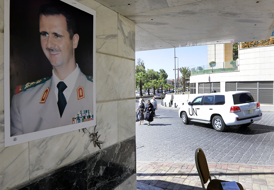 A poster of Syrian President Bashar al-Assad adorns a wall as a United Nations vehicle carrying inspectors from the Organisation for the Prohibition of Chemical Weapons leaves a hotel in Damascus, in October 2013.  (Photo by Louai Beshara/AFP via Getty Images)