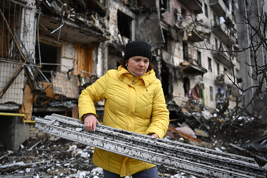 A woman clears debris at a residential building in a Kyiv suburb that was believed to be damaged by a military shell on February 25 after Russian forces reached the outskirts of the capital city. (Photo by Daniel Leal/AFP via Getty Images)
