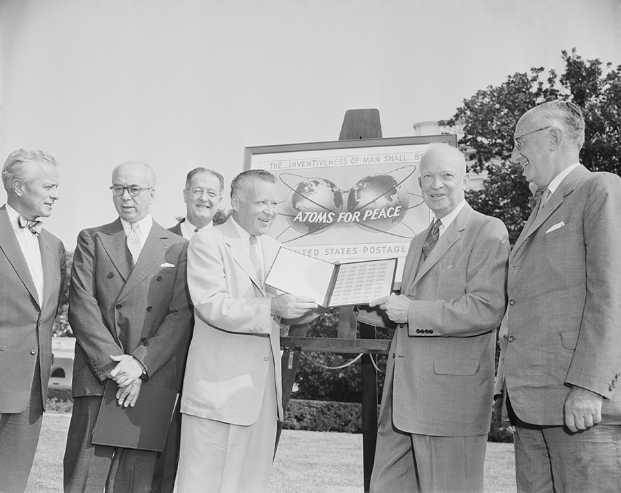 U.S. President Dwight Eisenhower (2nd from R) marks the issuance in 1955 of an “Atoms for Peace” commemorative stamp at the White House with, from left, Secretary of State John Foster Dulles, Chairman of the atomic Energy Commission Lewis Strauss, Senator Clinton Anderson (D-N.M.), Postmaster General Arthur Summerfield and Wilhelm Munthe de Morgenstierne, Norwegian ambassador to the United States. (Photo by Bettmann Archives via Getty Images)