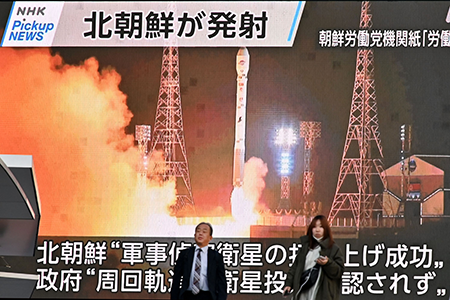Pedestrians walk past a video screen in Tokyo displaying the launch of North Korea's reconnaissance satellite 'Malligyong-1' on November 22, 2023.  (Photo by Kazuhiro Nogi/AFP via Getty Images)