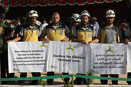 Syrian Civil Defense volunteers in 2025 hold a solidarity vigil in Zamalka with the families of the victims of the Aug. 21, 2013 chemical massacre in Syria. On that date, President Bashar al-Assad ordered strikes on two opposition-controlled areas of Ghouta. The rockets contained the chemical nerve agent Sarin that killed hundreds of people. (Photo by Ali Haj Suleiman/Getty Images)